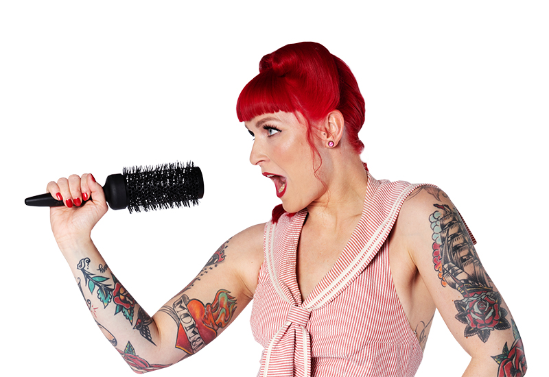 frau-mit-rot-gefaerbten-haaren-tattoos-an-beiden-armen-singt-mit-buerste-in-der-hand