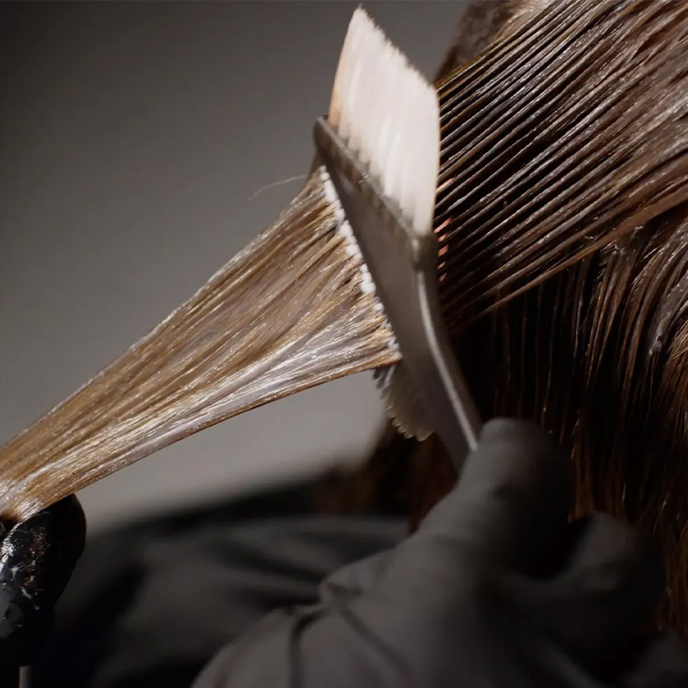 revlon-friseur-traegt-haarfarbe-mit-pinsel-auf-eine-straehne-auf-und-arbeitet-die-farbe-gleichmaessig-ins-haar-ein