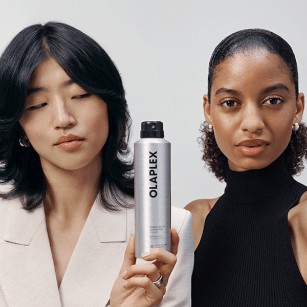 Zwei Frauen mit dunklem Haar und einer silberfarbenen Dose OLAPLEX Shape Set Hairspray