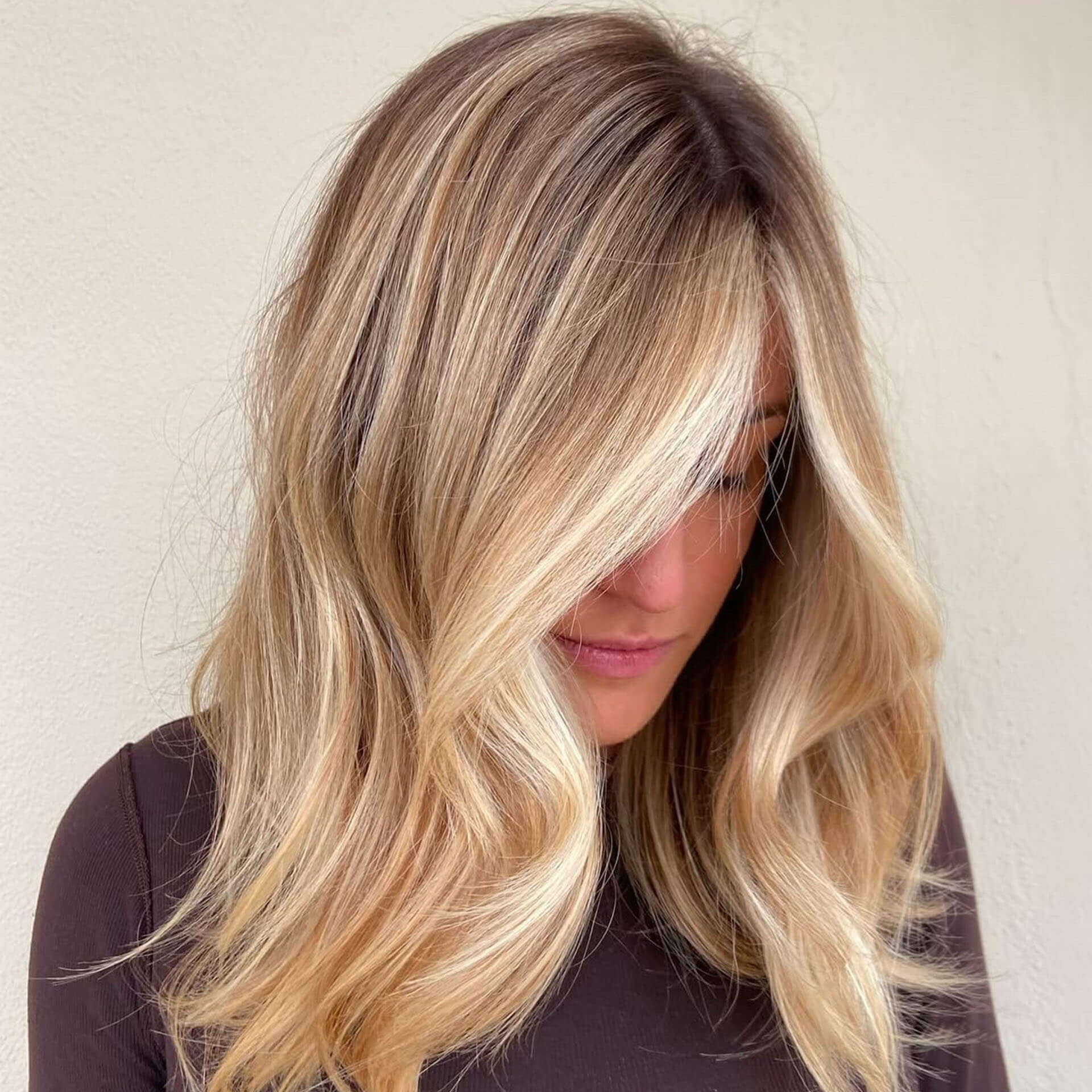 frau-mit-schulterlangem-blondem-haar-und-weichen-beachwaves-schaut-nach-unten-vor-heller-wand