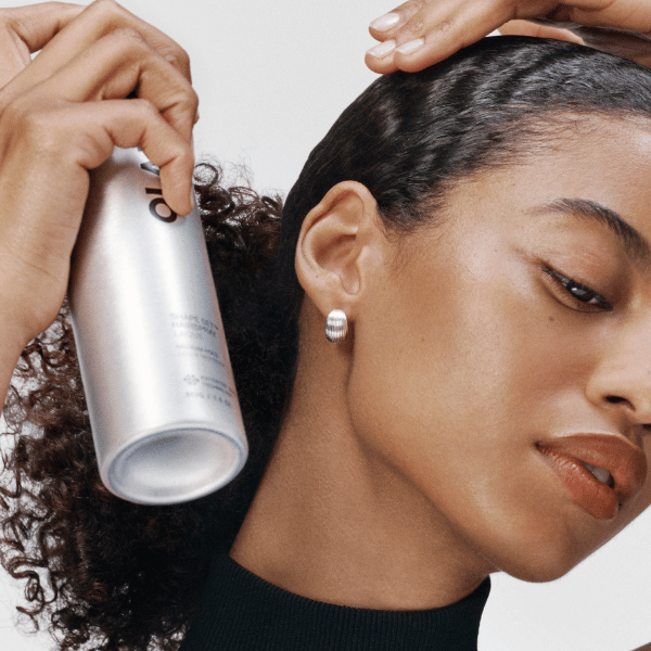 OLAPLEX Shape Set Hairspray wird am seitlich glatt angelegten Haar einer Frau mit lockigem Zopf angewendet