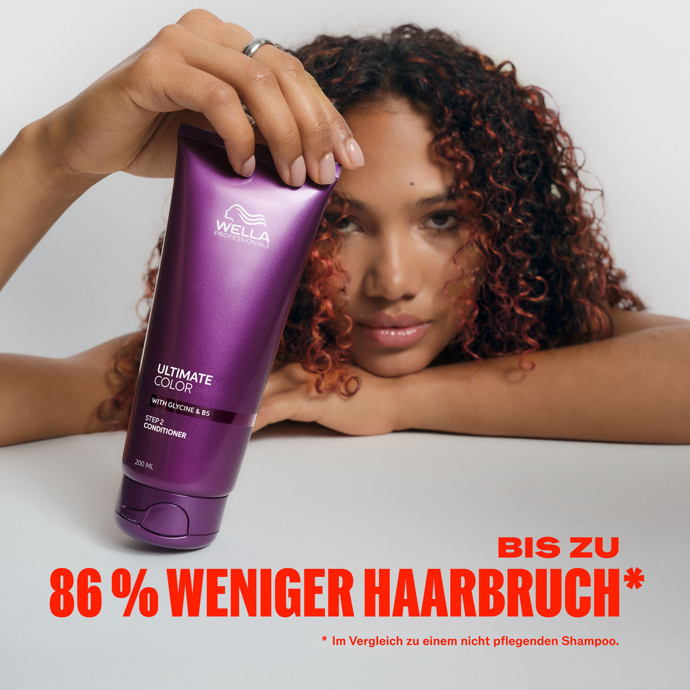 frau-mit-lockigem-haar-haelt-wella-ultimate-color-conditioner-tube-vor-dem-gesicht-mit-text-zu-86-prozent-weniger-haarbruch